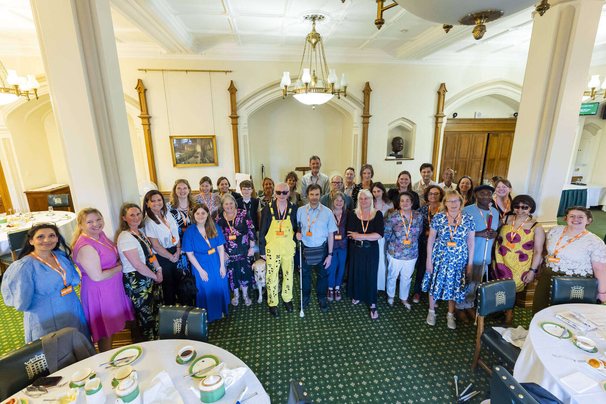 All workshop participants standing in a half circle looking towards the camera. The room in the background is decorated in green, crème and wooden colours.