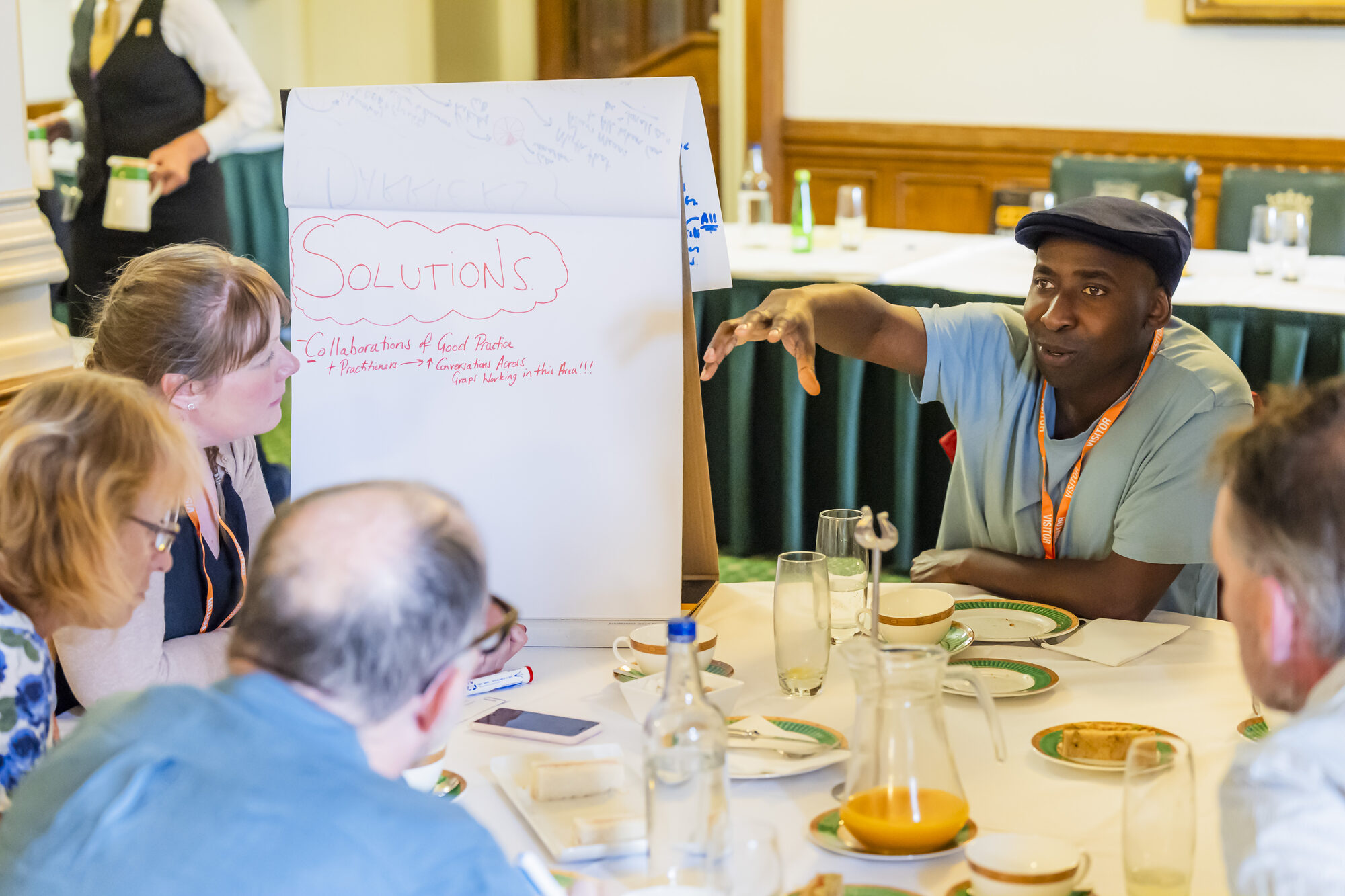 Co-investigator Dr Leighanne Higgins is sitting at a round white table with fellow workshop participants. They seem to be involved in a vivid discussion. Leighanne is taking notes on a flip chart.